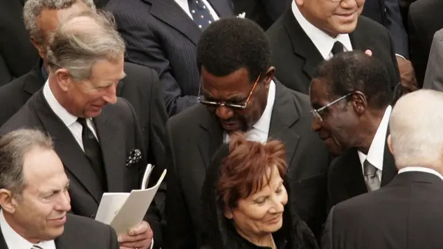 Charles wearing a black suit talking to Mugabe