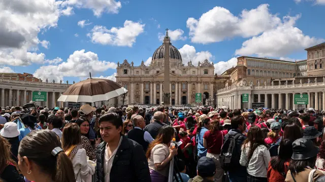 Crowds gather outside St Peter's Basilica on a bright day with blue skies.