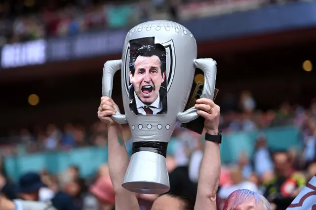 A fan of Aston Villa holds up an inflatable FA Cup with a picture of Unai Emery attached