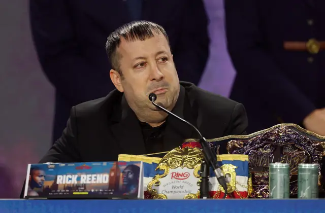 Rick Reno sits at the top table of a boxing news conference with the Ring Magazine title inf ront of him