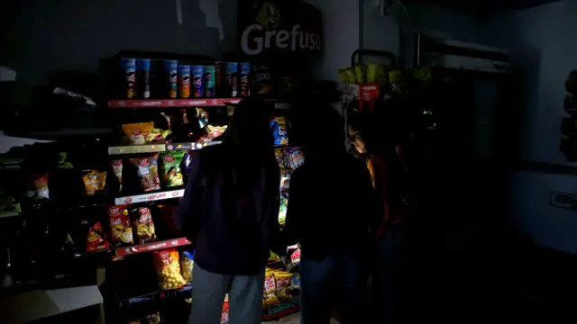 The outline of three people in darkness as they shine phone torches at shelves of crisps
