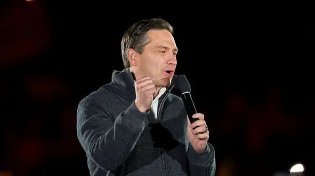 Headshot of Poilievre speaking as he holds a microphone and has a fist raised