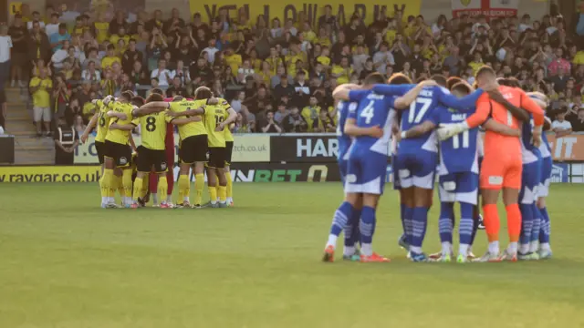 Burton and Wigan players huddle before kick-off
