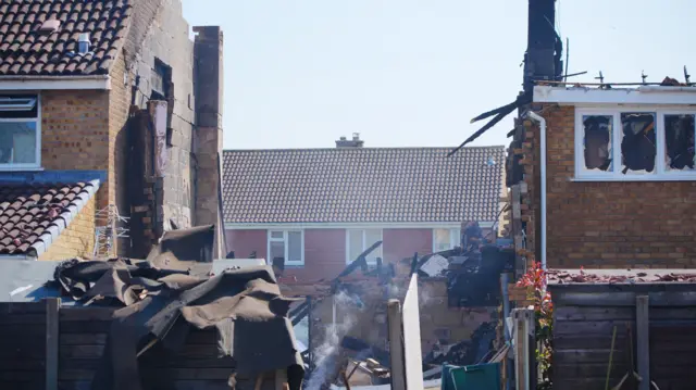 The middle house in a row of terraced properties has been completely blown out, with smoking remains and crumpled debris laying strewn about.