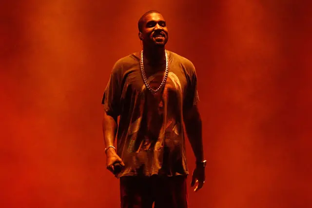Kanye West on stage wearing a large silver chain with a red background