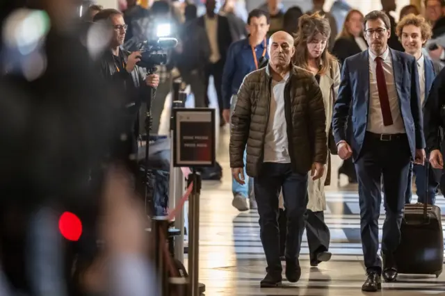 Paparazzo taking a photo of Yunice Abbas and his lawyer as they enter the court