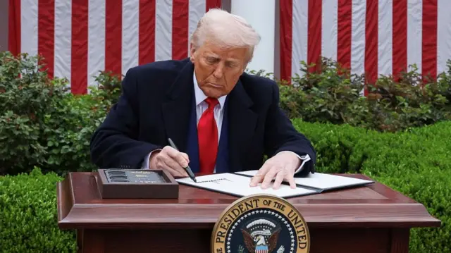 Trump sits at a desk outside and signs an executive order