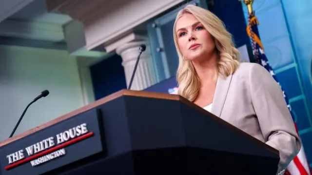 A low-angle shot of Leavitt, who stands at the White House lectern looking stern