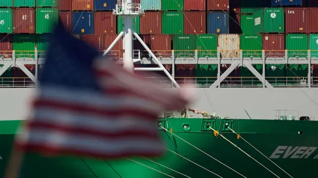 Trade containers on a ship with a blurred US flag in the foreground