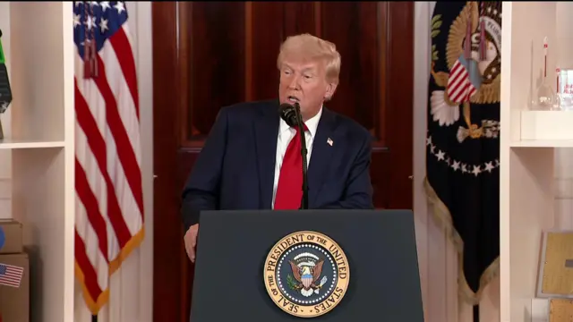 Donald Trump wearing a red tie speaking at a podium