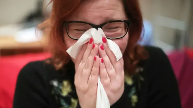 A woman sneezing into a tissue