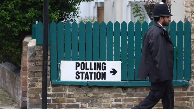 A polling station is seen with a man in a police uniform walking in front of it