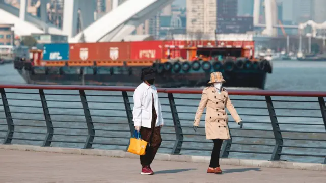 People walk on the river bank while cargo ships sail on the Huangpu River in Shanghai