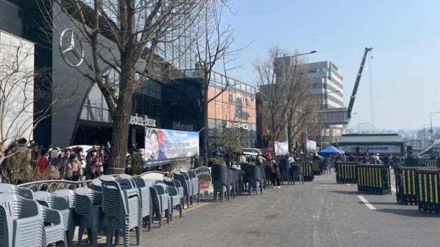 An empty, barricaded road. Chairs are stacked neatly on one side.