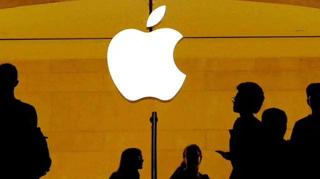 An Apple logo shines at the centre of the image against an orange background. The darkened outlines of people are below the logo