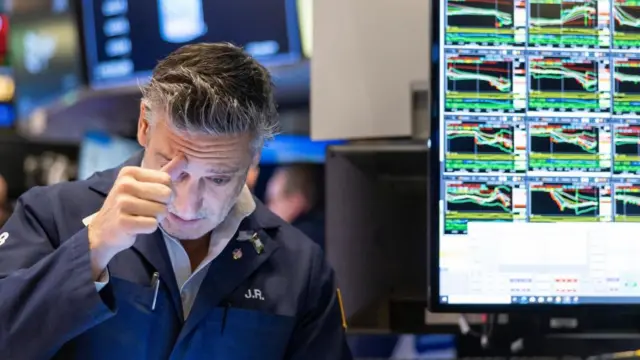 A trader looks concerned at his screen with a screen showing various charts in the background.