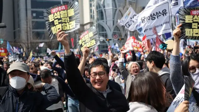 A man smiles as he raises a poster, surrounded by protesters