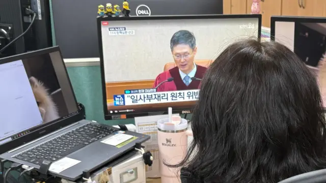 Backview of a woman at her desk looking at a computer screen showing the constitutional judge reading the verdict