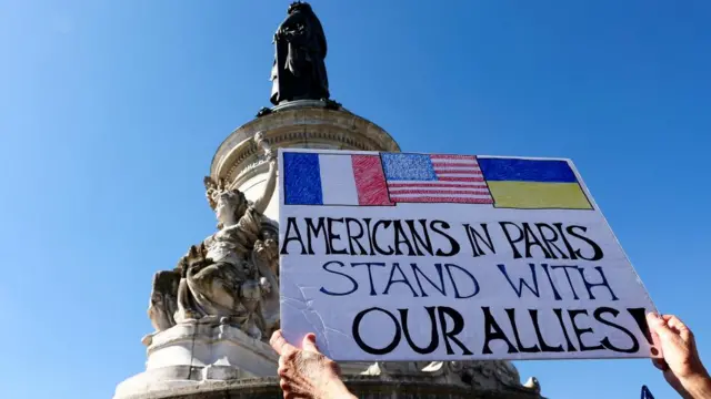 A person holds a placard in Paris reading: Americans in Paris stand with our allies!