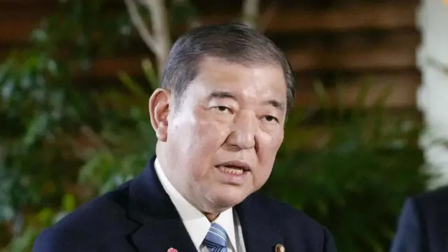 PM Shigeru Ishiba speaks in a suit with plants in the background.