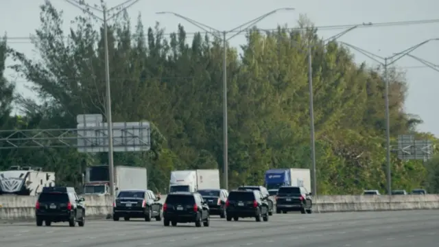 The motorcade of US President Donald Trump arrives at his golf course in Jupiter, Florida. Several black SUVs are driving on a motorway.