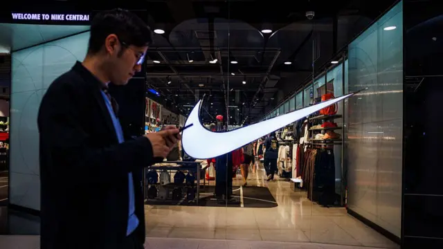 Man texting on phone as he walks in front of Nike shop with large Nike tick on the windows