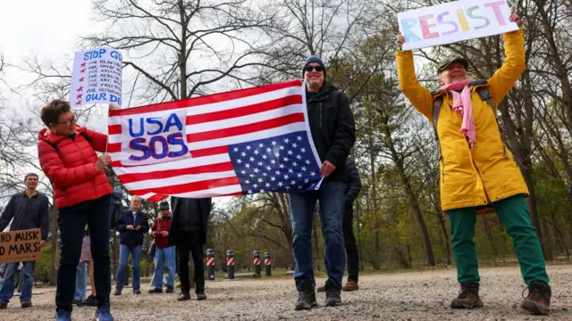 Demonstrators hold an upside-down US flag reading USA SOS, and another holds a sign saying: Resist.