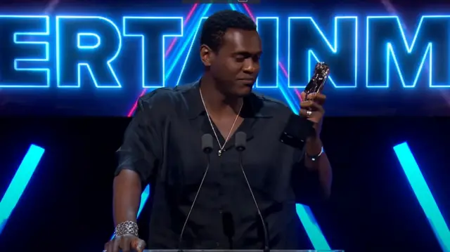Abubakar Salim standing on stage looking down at award
