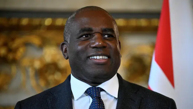 David Lammy smiles in a dark suit and blue tie.