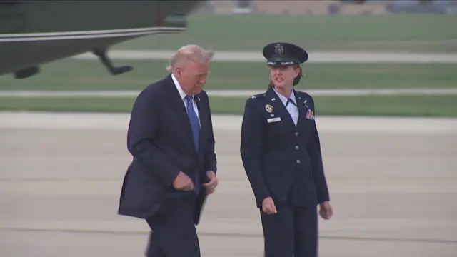 Donald Trump walking on tarmac at an airport with a woman in uniform beside him