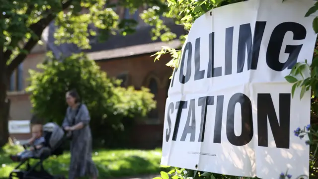 A voting station sign with a mother and child in the background