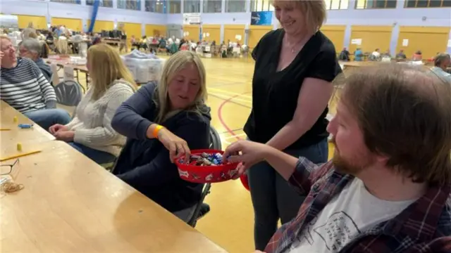 Two people are grabbing chocolates from a box another person is handing them.