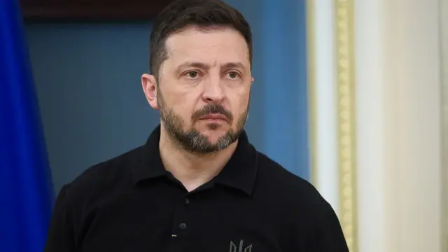 President of Ukraine Volodymyr Zelensky, who has short black hair with a beard, wearing a black button up top.