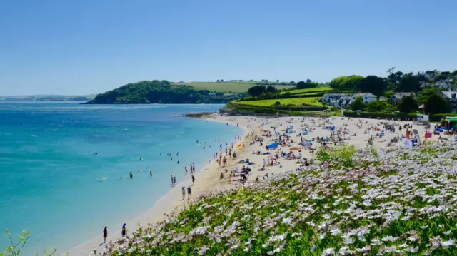 A crowded beach with blue skies on a sunny day in Cornwall.