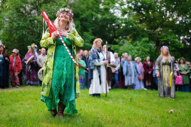 A woman wears a flower crown and holds a staff
