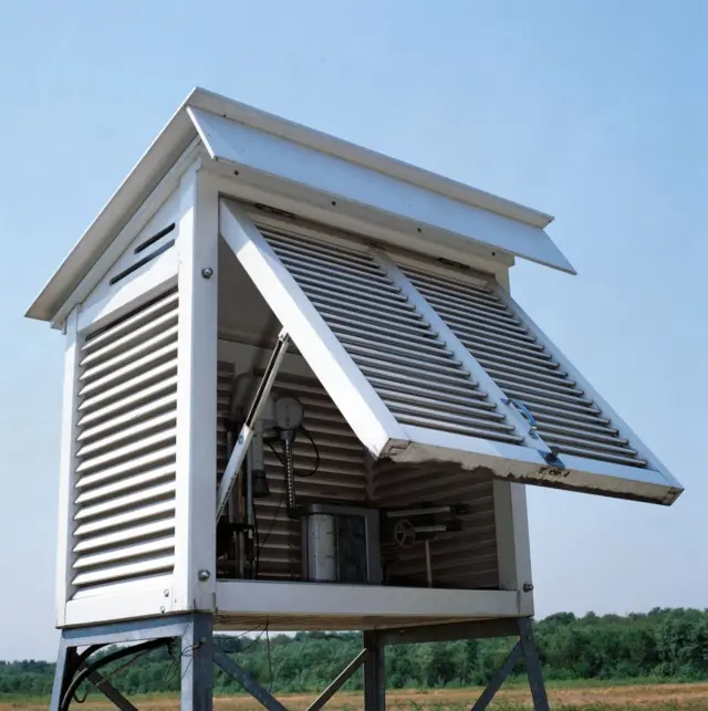 A Stevenson Screen - a white box with ventilation slats that allows the temperature to be taken in the shade. It is in a field.