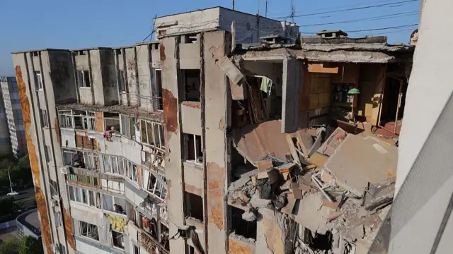 Local residents look out of broken windows in a damaged residential building following a drone attack in Odesa
