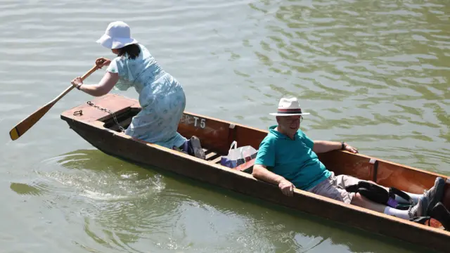A woman holds an oar, while a man sits in a punt