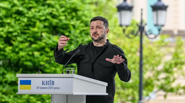 Zelensky speaks behind a podium in Kyiv, wearing black clothes.