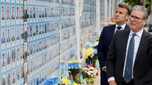 Emmanuel Macron (background L) and Keir Starmer (foreground R) stand in front of a wall carrying the pictures of fallen Ukrainian soldiers