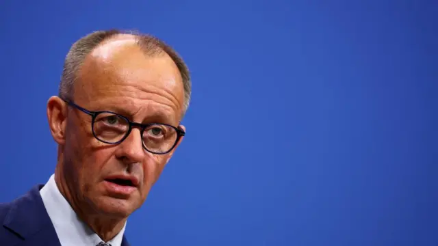 German Chancellor Friedrich Merz speaks wearing a suit and glasses