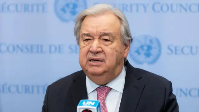 Antonio Guterres speaks from behind a microphone in front of a UN banner.