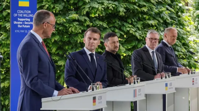 Merz, Macron, Zelensky, Starrer, Tusk speak behind white podiums with microphones in Kyiv.
