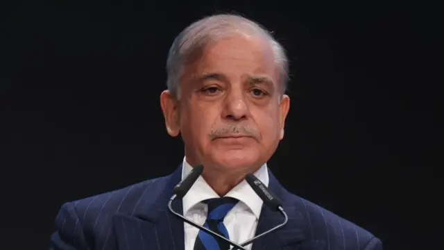 Pakistan's prime minister wears a suit behind a microphone.