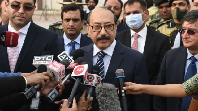 Harsh Vardhan Shringla stands surrounded by reporters holding microphones.