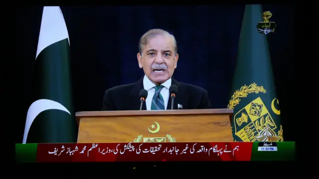 Sharif stands at a lectern in a suit and tie while speaking into a microphone.