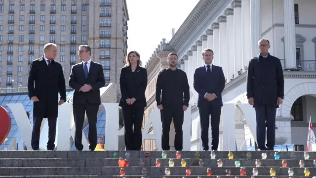 German Chancellor Friedrich Merz, French President Emmanuel Macron, Ukrainian President Volodymyr Zelenskiy and his wife Olena Zelenska, Britain's Prime Minister Keir Starmer, and Poland's Prime Minister Donald Tusk visit Maidan Square. They stand, wearing formalwear, and look ahead.
