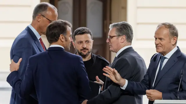 Merz. Macron, Zelensky, Starmer, and Tusk all stand together talking to each other following delivering a press conference.