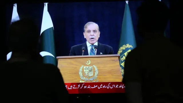 Sharif stands at a lectern in a suit and tie while speaking into a microphone.