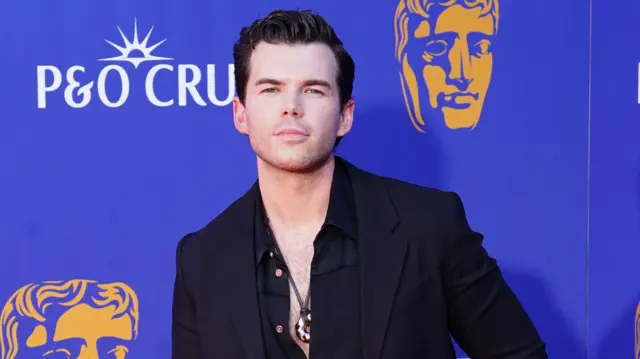 Luke Newton in a black suit